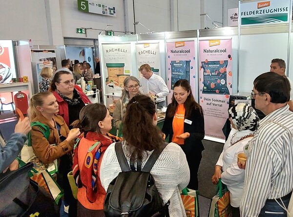 Leute hören vor einem Messestand einer Frau zu