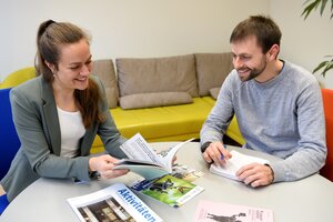 Eine Frau und ein Mann sitzten an einem Besprechungstisch und schauen sich Broschüren an