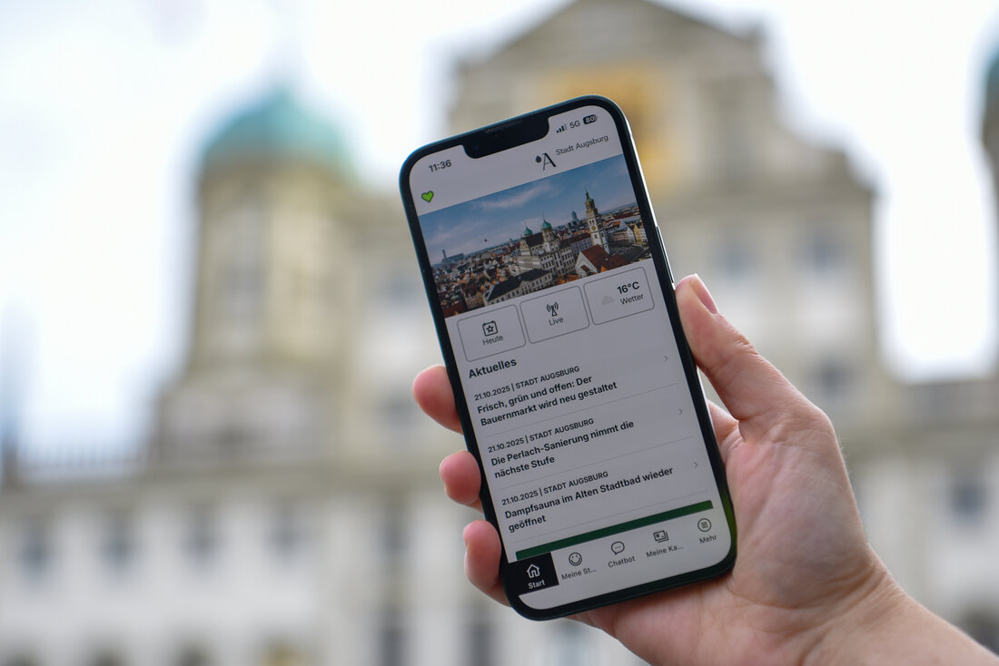 Bild zeigt Handy mit App vor dem Augsburger Rathaus.
