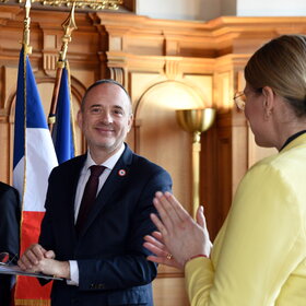 Drei Personen im Rathaus. Im Hintergrund die französische Flagge