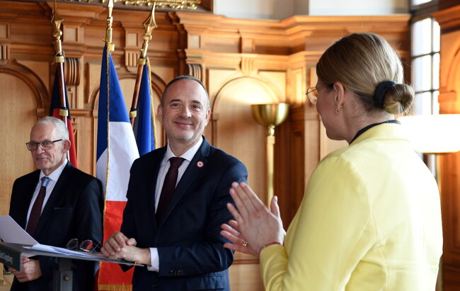 Drei Personen im Rathaus. Im Hintergrund die französische Flagge