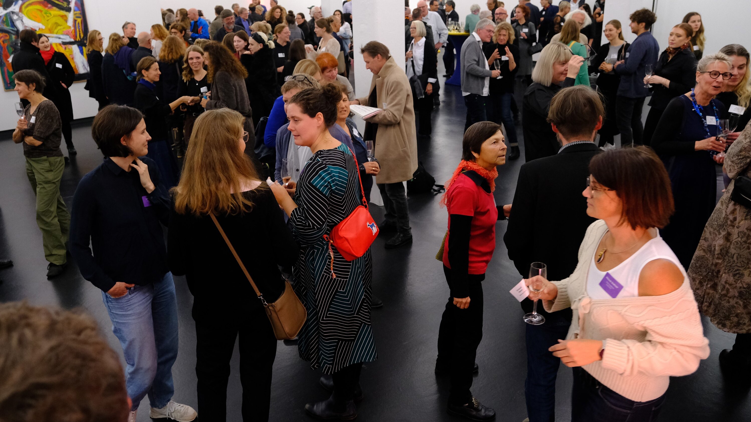 In einer modernen Halle mit Säulen stehen viele Menschen in Gruppen zusammen und unterhalten sich angeregt