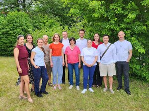 Gruppenfoto vor Bäumen auf einer Wiese mit 12 Personen die versetzt nebeneinander stehen