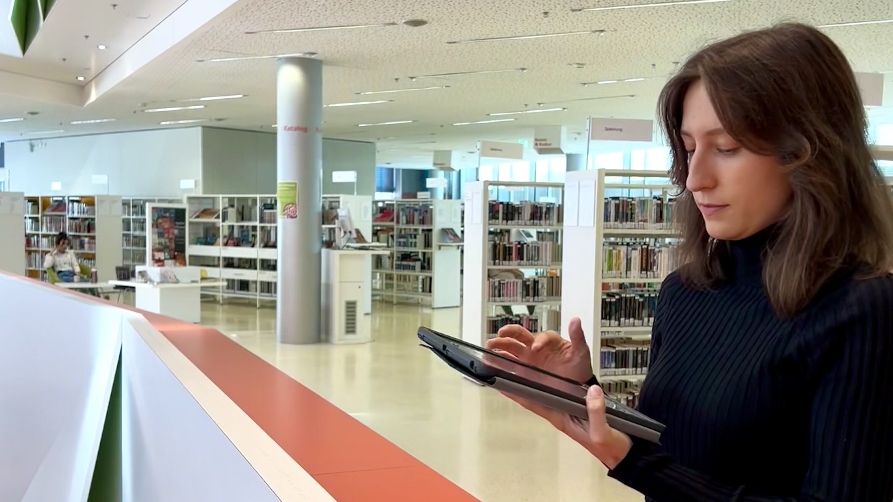 Eine Frau steht mit einem Tablet in der Stadtbücherei
