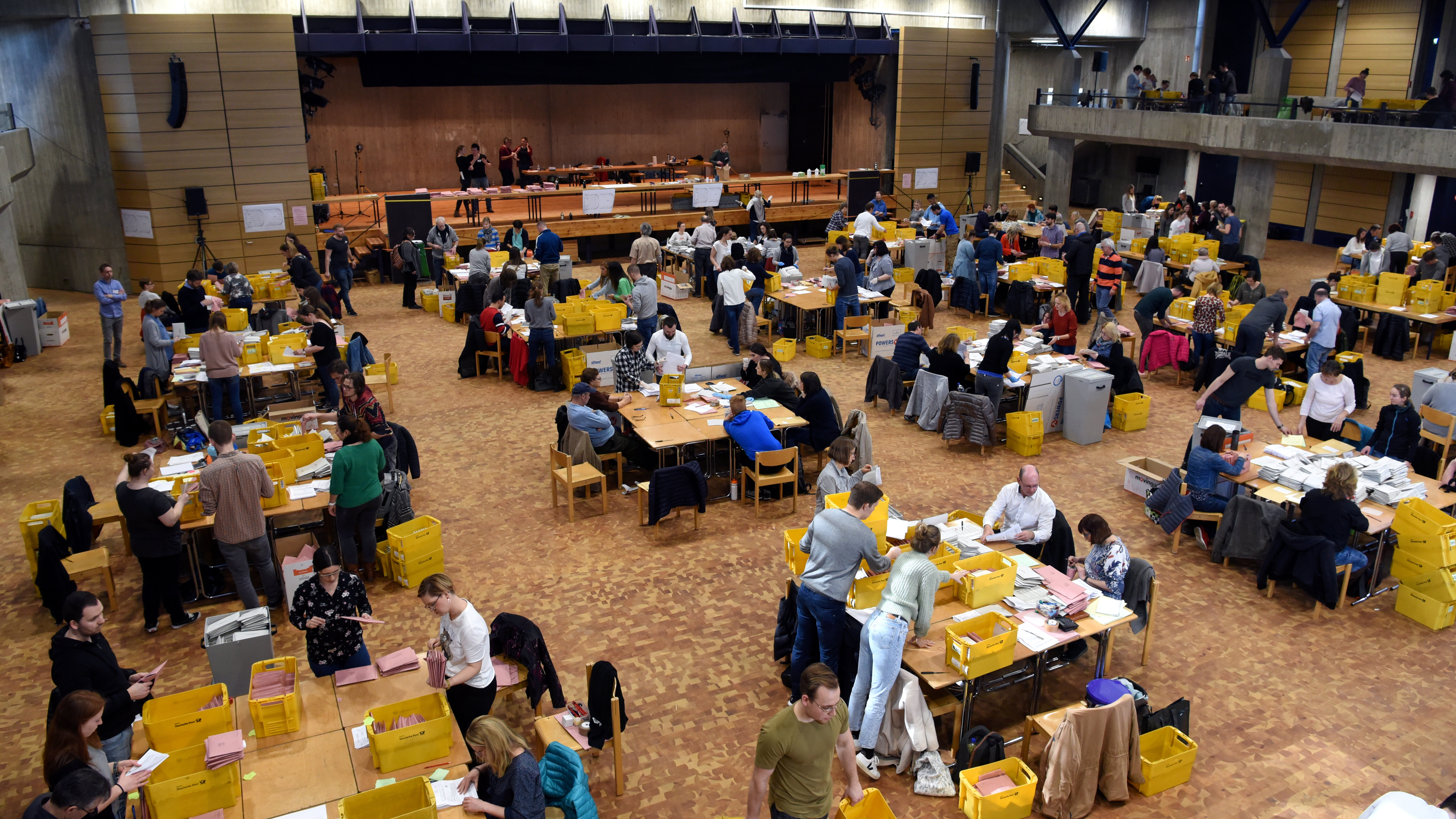 In einem großen Saal sitzen viele Leute an Tischen und zählen Briefe und Zettel