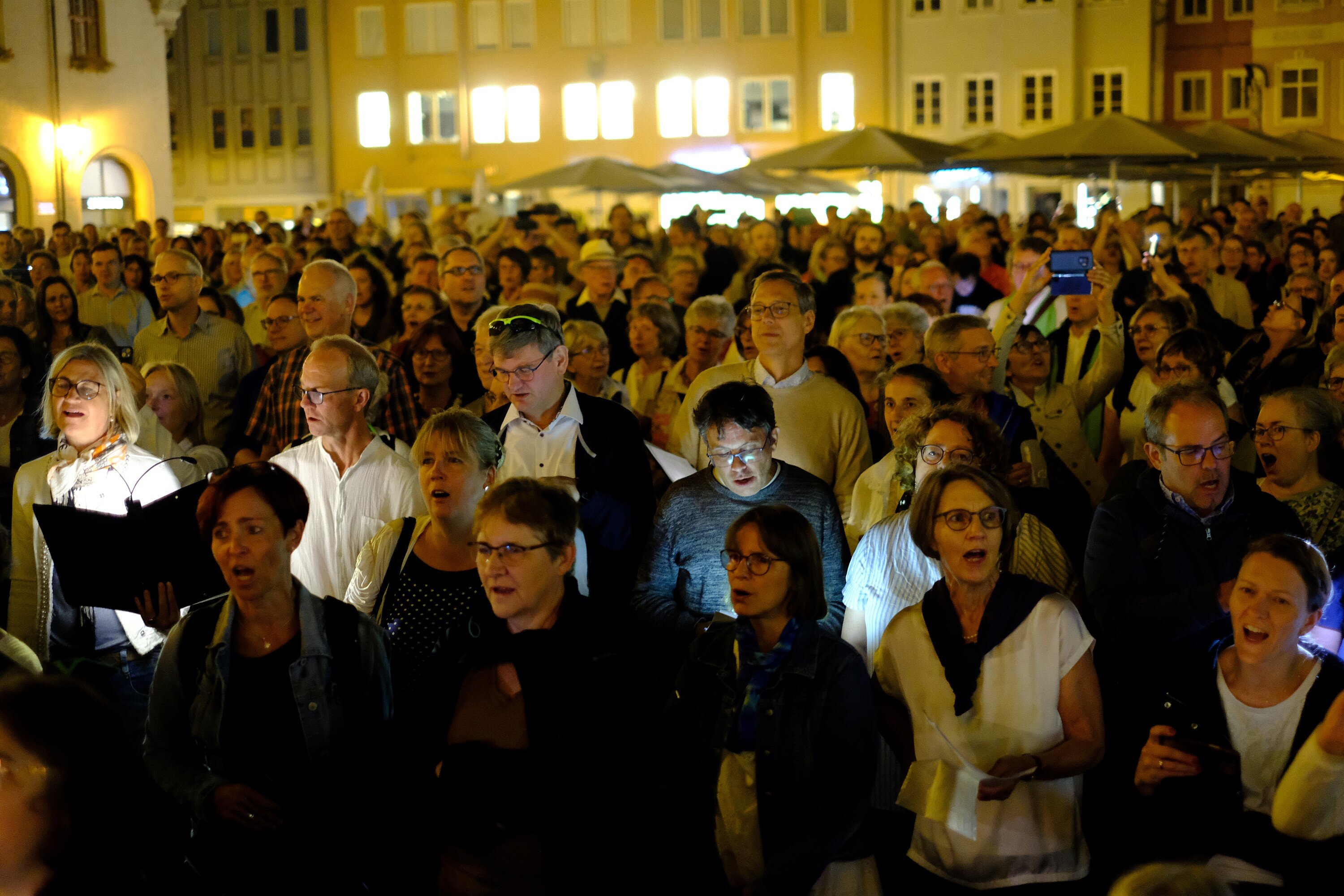 Viele Leute stehen bei Nacht auf dem Rathausplatz und singen gemeinsam