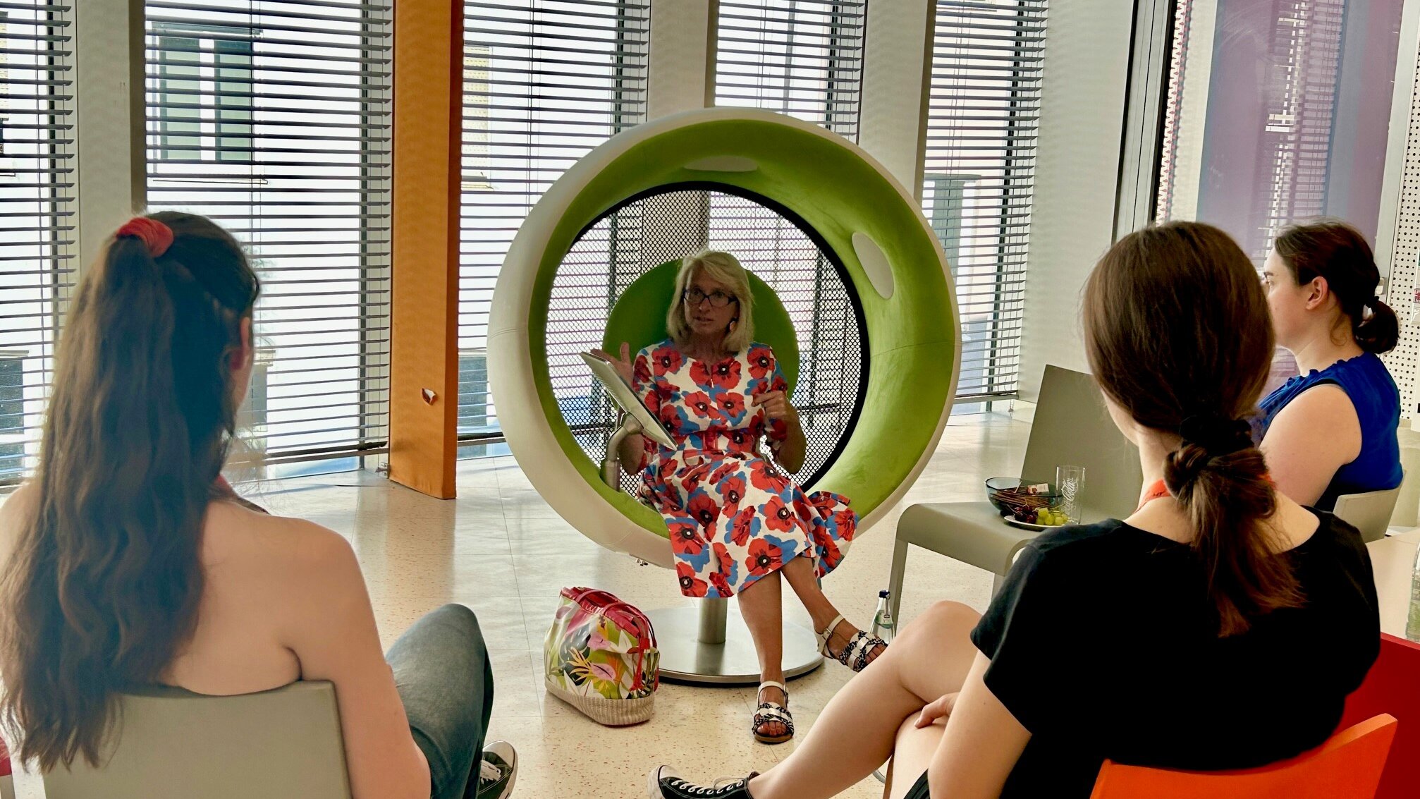 Drei Personen sitzen in der Stadtbücherei und hören einer Frau zu.