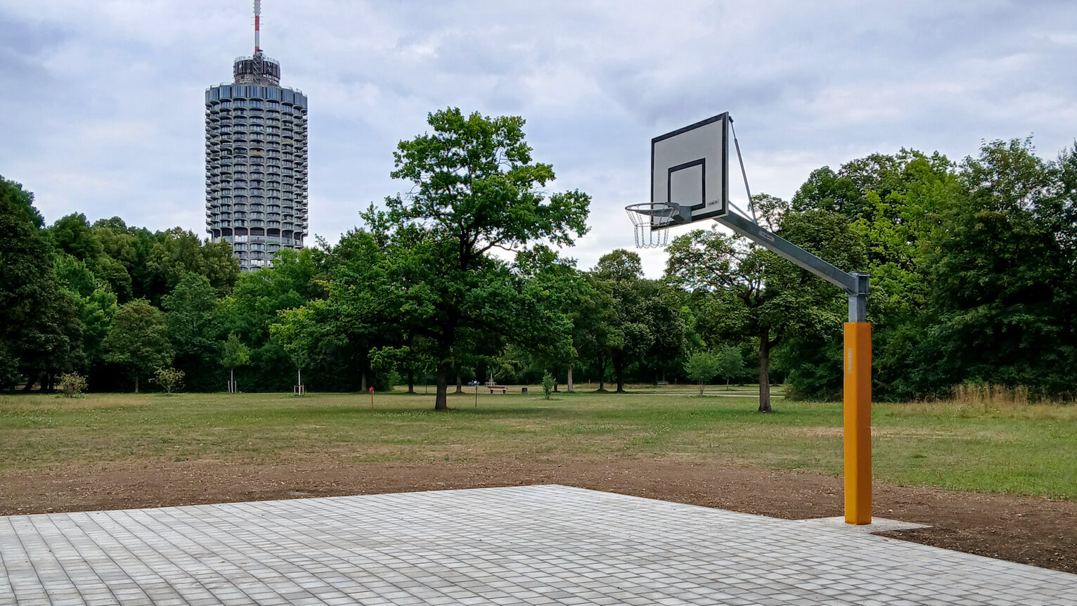 gepflasterte Fläche mit Basketball-Korb umgeben von einer Wiese, im Hintergrund der Hotelturm