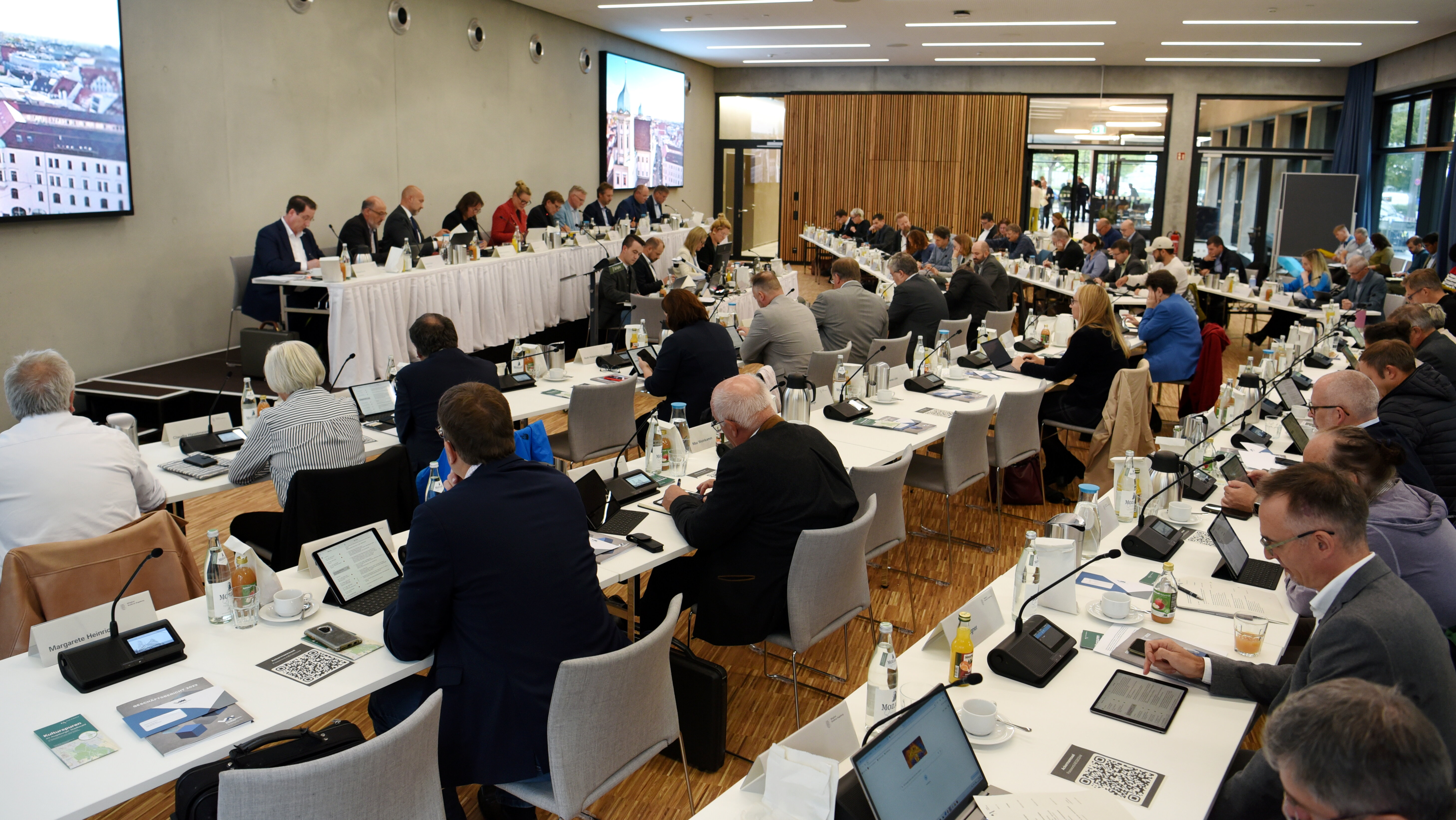 In einem großen Rauf stehen viele Tische. Daran sitzen die Mitglieder des Stadtrats