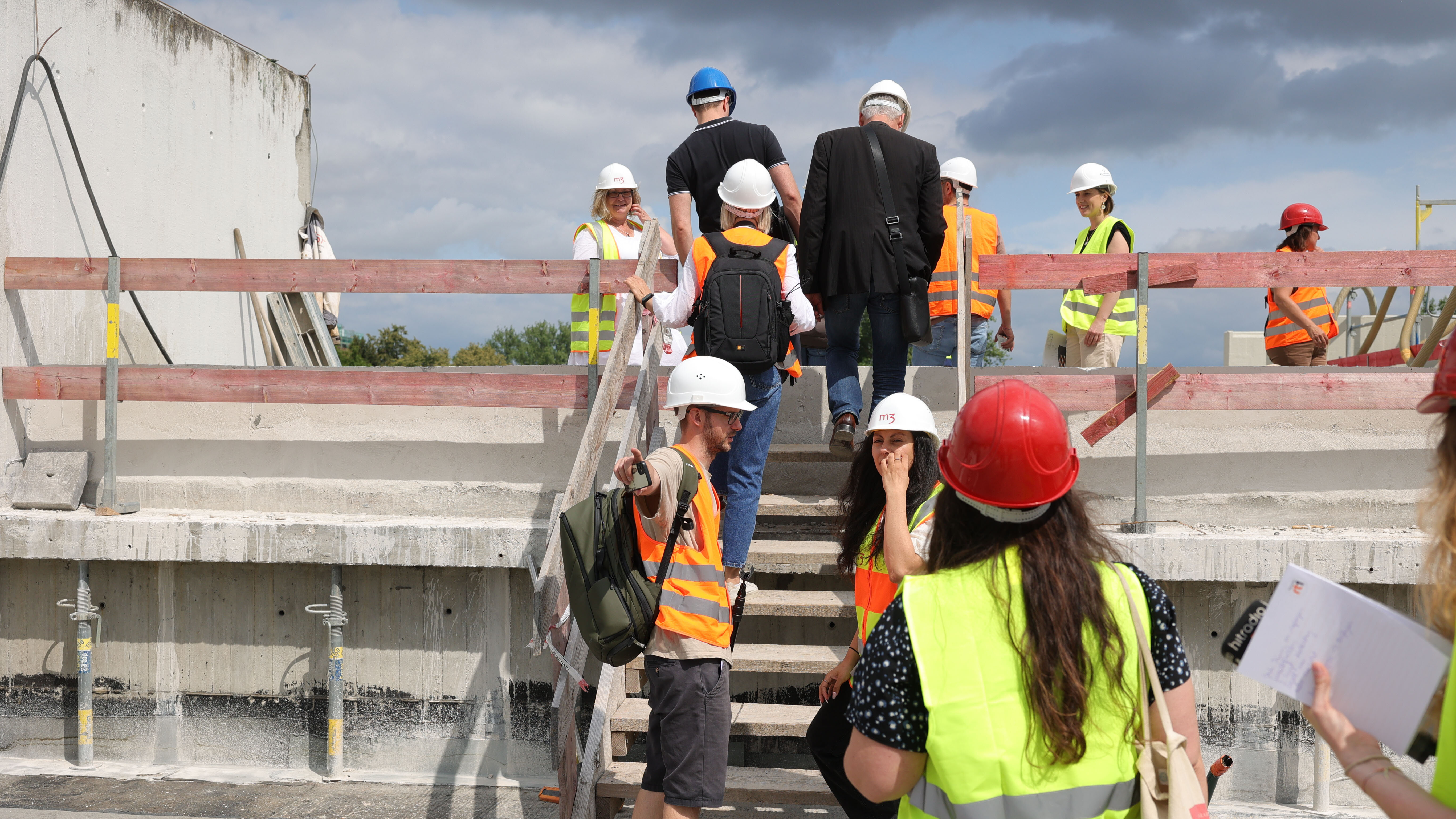 Mehrere Menschen mit Baustellenhelmen und Warnwesten laufen über eine Baustelle