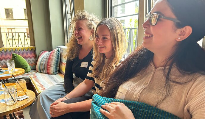 3 Frauen sitzen auf einer Bamk im Café und lachen