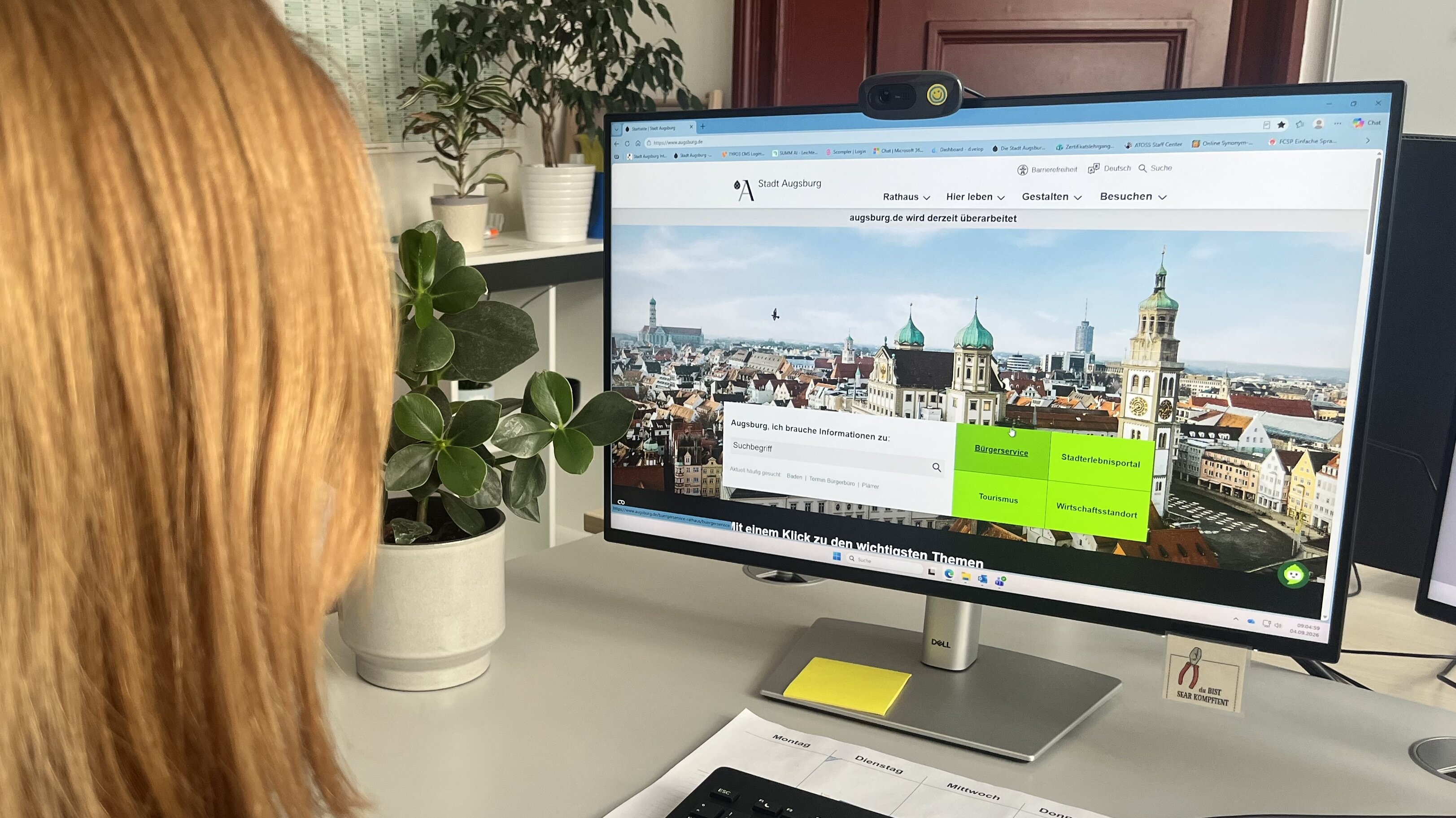 Eine Frau sitzt am Computer. Auf dem Bildschirm ist augsburg.de zu sehen
