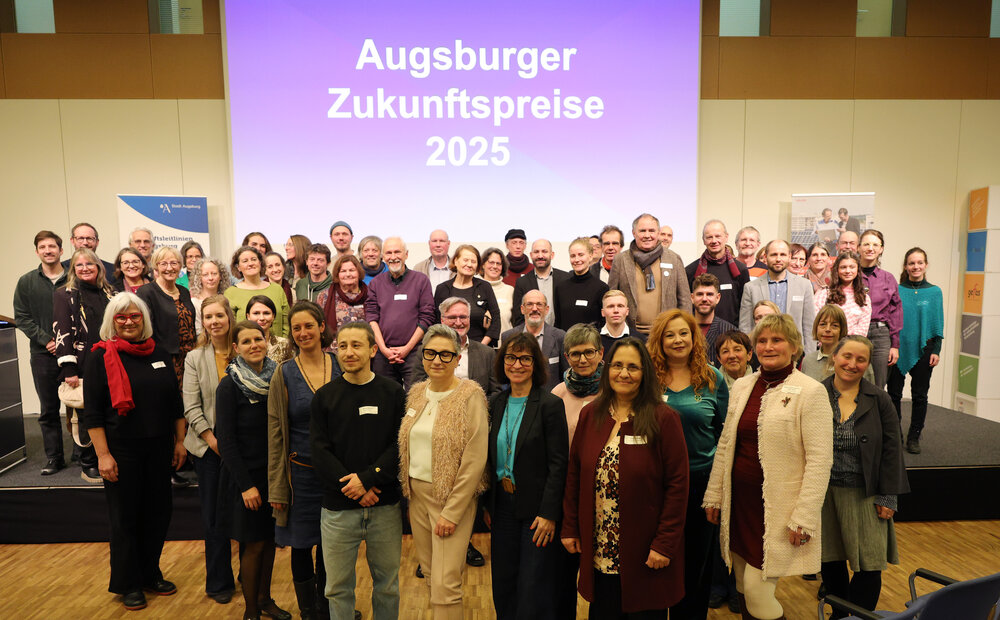 Gruppenbild, im Hintergrund eine Wandprojektion mit der Schrift "Augsburger Zukunftspreise 2025"