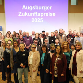 Gruppenbild, im Hintergrund eine Wandprojektion mit der Schrift "Augsburger Zukunftspreise 2025"