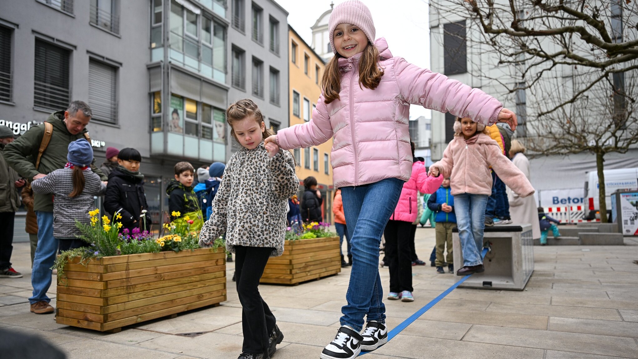 Auf dem Foto ist eine Slackline zu sehen. Darauf balanciert ein Mädchen und strahl in die Kamera. An der Seite hält ein anderes Mädchen ihre Hand.