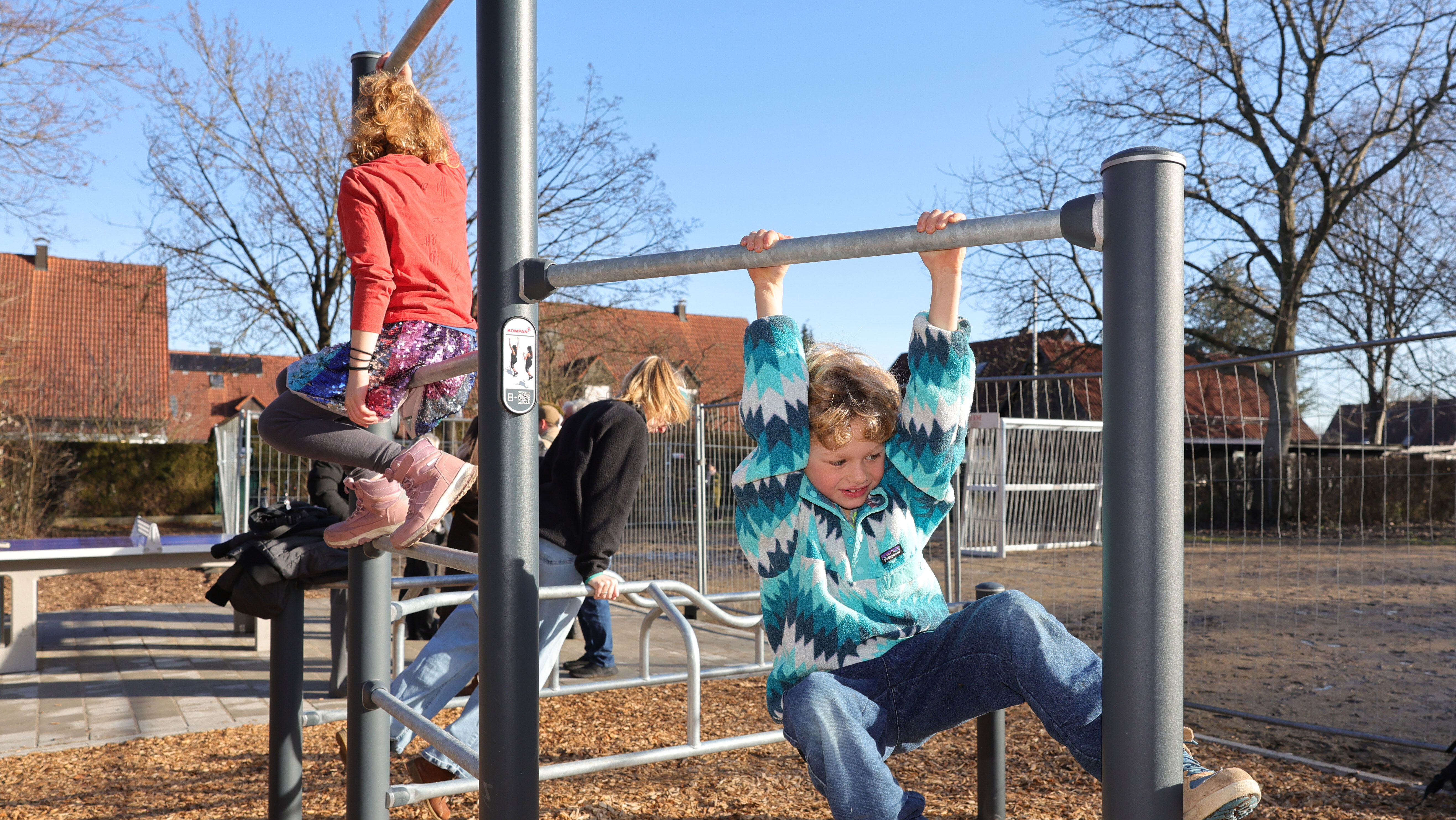 Kinder spielen an einem Klettergerüst. Ein junge hängt im Vordergrund an einer Reckstange. Ein Mädchen klettert im Hintergrund.