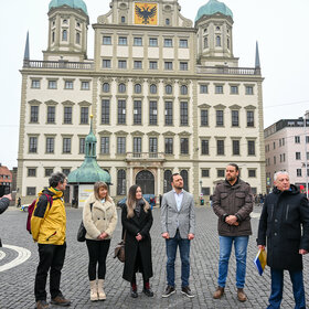 Das Foto zeigt Vertreterinnen und Vertreter der Stadt Augsburg und Perwomajsk. Sie stehen auf dem Rathausplatz. Im Hintergrund ist das Augsbruger Rathaus zu erkennen