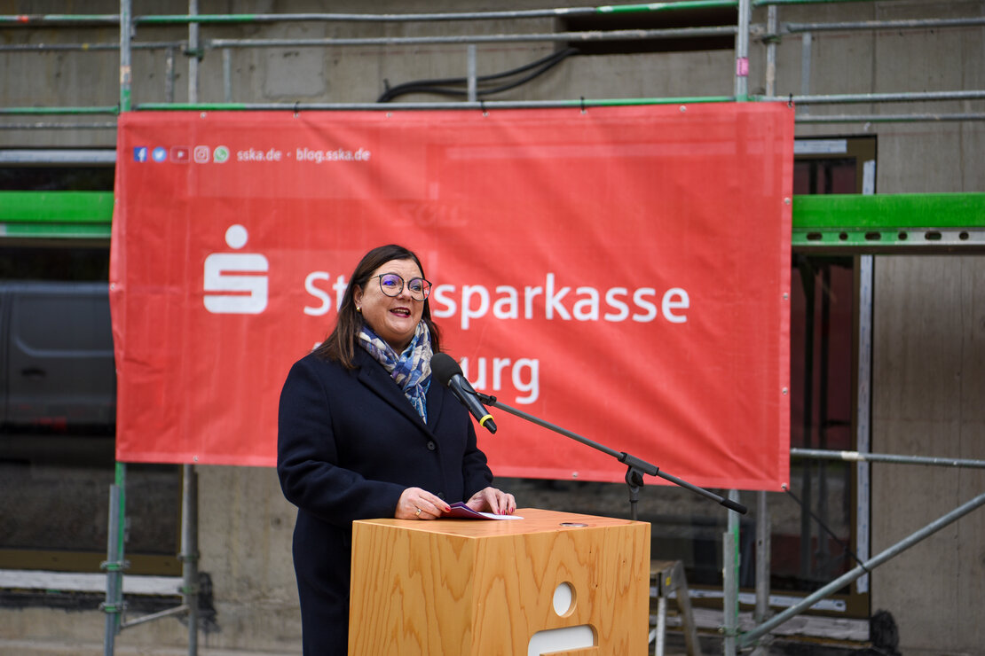 Rednerein am Pult, sdahinter ein Banner der Stadtsparkasse Augsburg