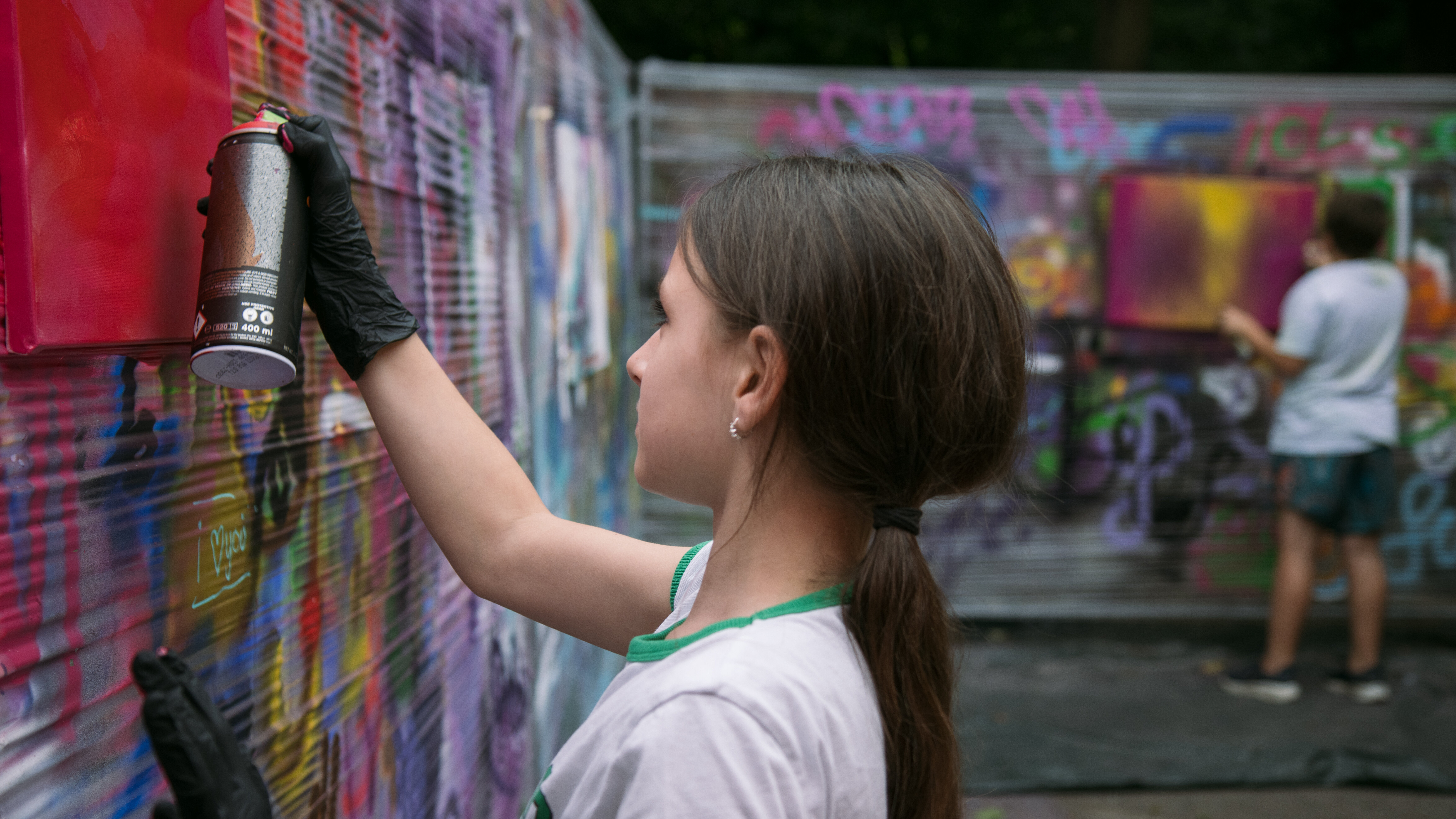 Ein Mädchen sprüht mit einer Spraydose ein buntes Bild an eine Graffiti-Wand