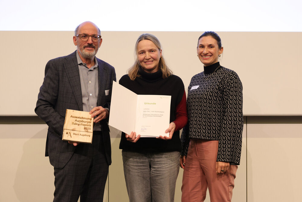 Gruppenbild dreier Personen, die gemeinsam eine Urkunde in die Kamera halten