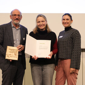 Gruppenbild dreier Personen, die gemeinsam eine Urkunde in die Kamera halten