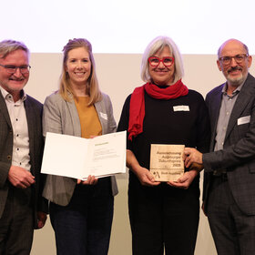 4 Personen halten eine Urkunde in die Kamera