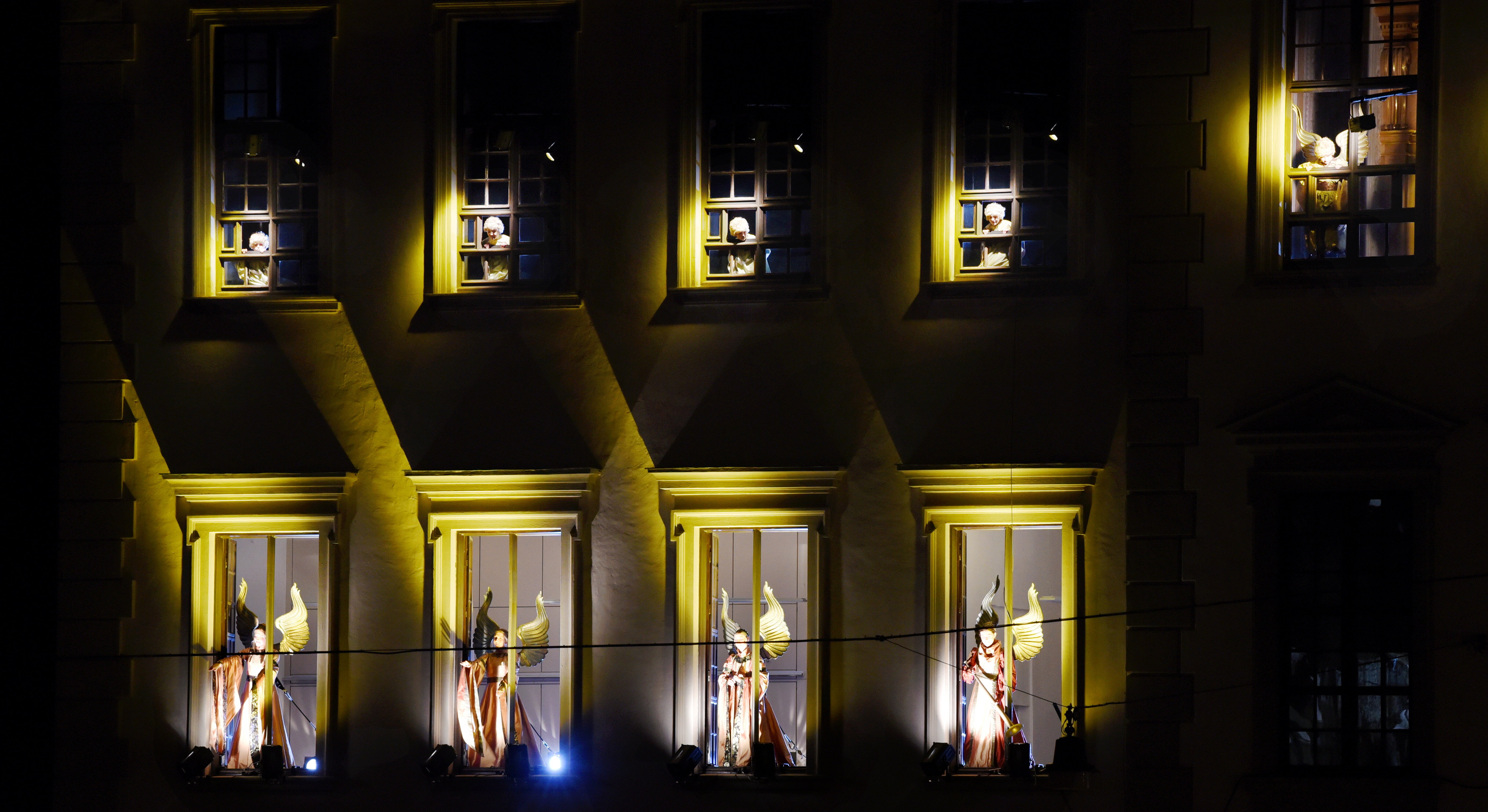 Bei Nacht: Als Engel verkleidete Menschen, stark beleuchtet in den Fenstern des Rathauses.