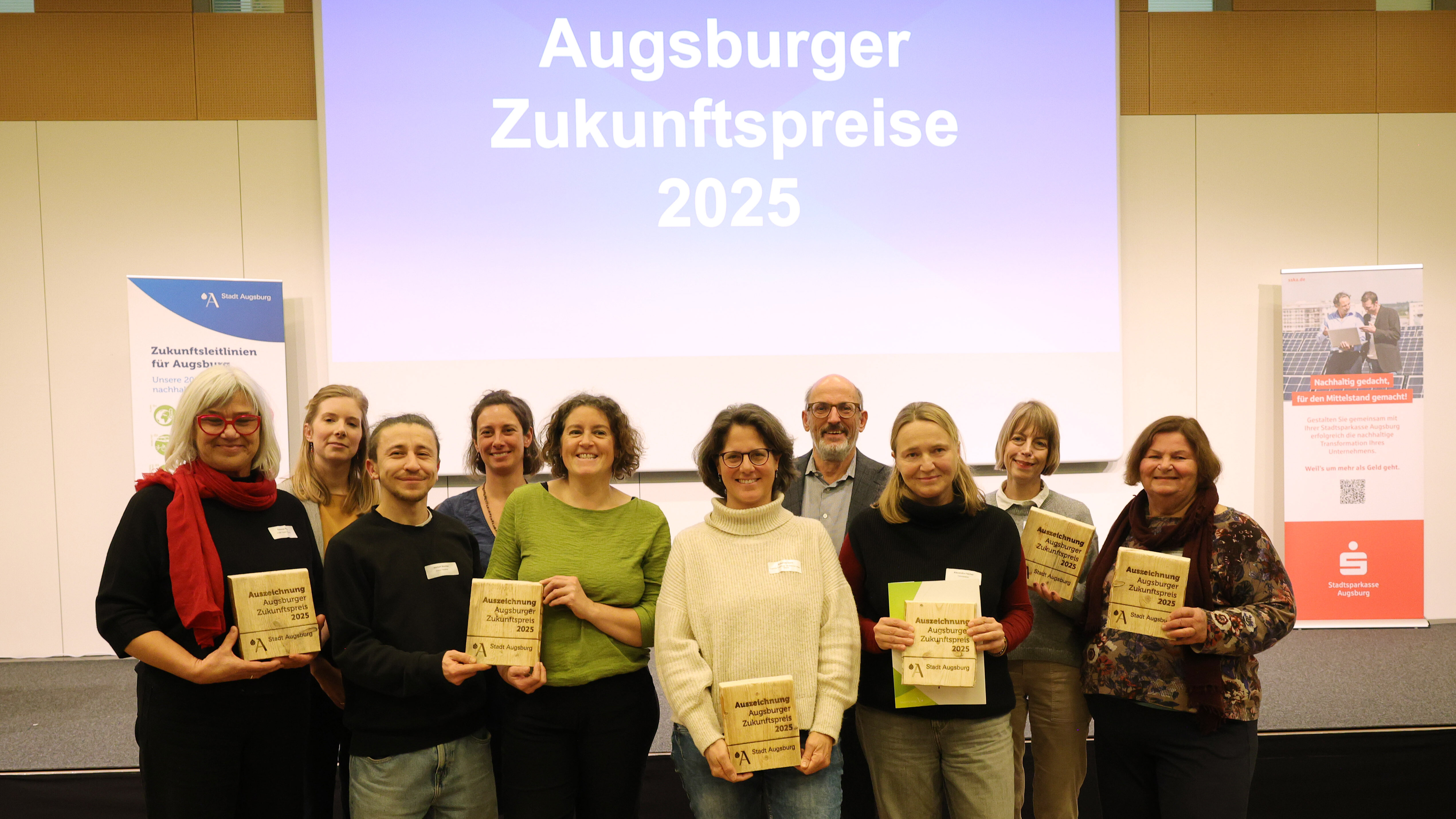 Zehn Menschen, die meisten halten eine Auszeichnung in der Hand. Im Hintergrund steht "Augsburger Zukunftspreis 2025"