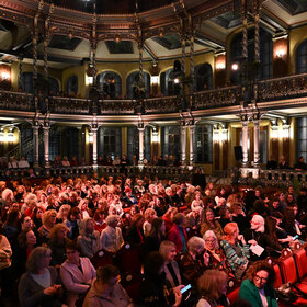 Das Foto zeigt viele Frauen in einem prunkvollen und abgedunkelten Saal sitzen