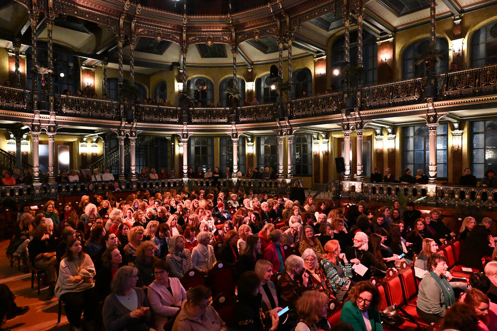 Das Foto zeigt viele Frauen in einem prunkvollen und abgedunkelten Saal sitzen