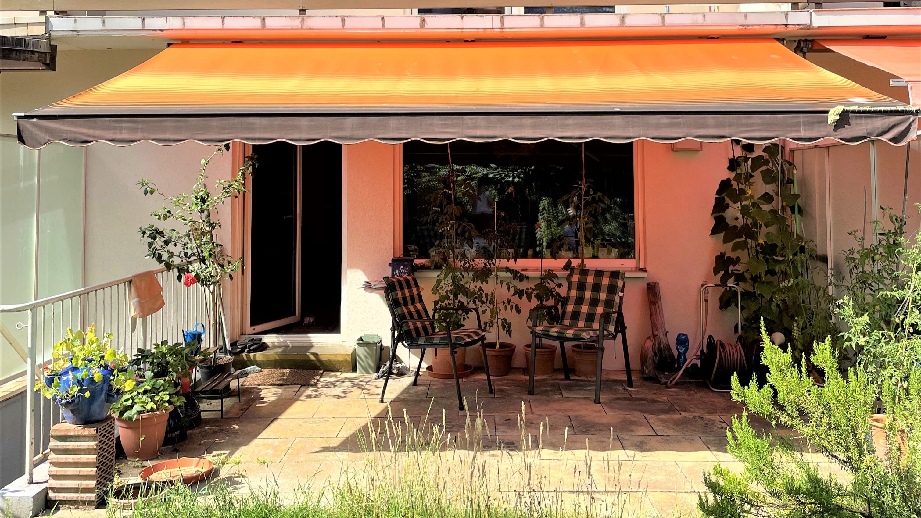 Blick auf Terrasse eines typischen Reihenhauses vom Garten aus, die Terrasse wird von einer Markise beschattet