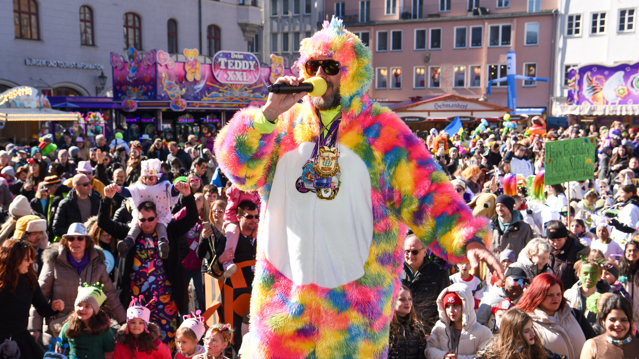 Mann in buntem Kostüm. Im Hintergrund viele verkleidete Menschen.