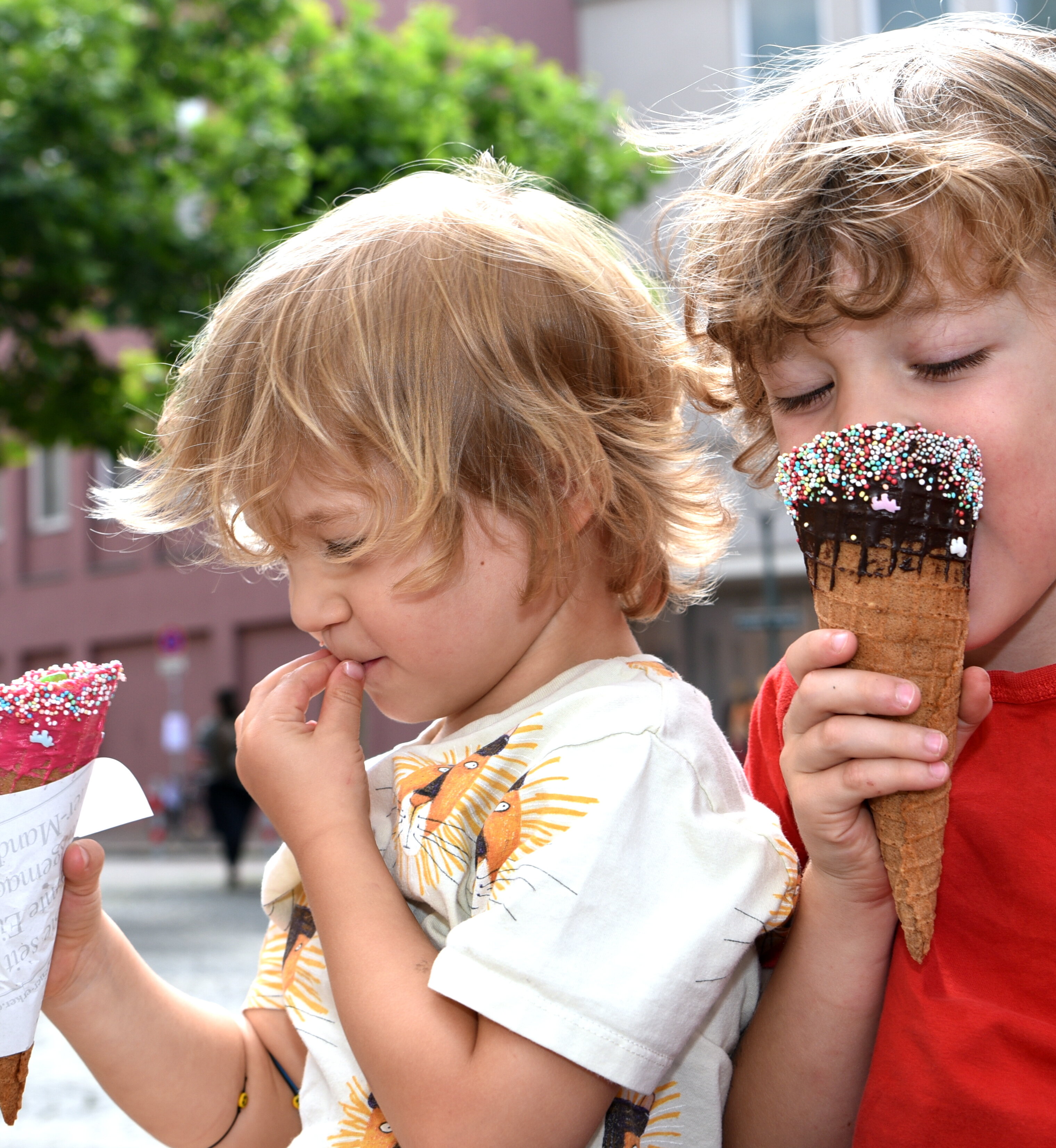 2 Kinder essen Eistüten, im Hintergrund ein Laubbaum