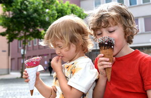 2 Kinder essen Eistüten; im Hintergrund ein Baum