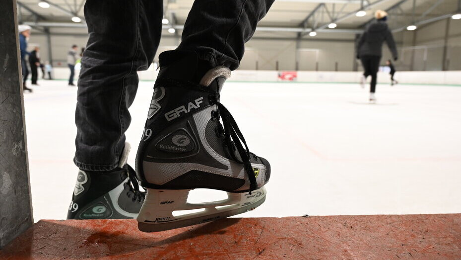 Zu sehen sind die Beine eines Eisläufers mit Schlittschuhen, der gerade auf die eisbahn geht