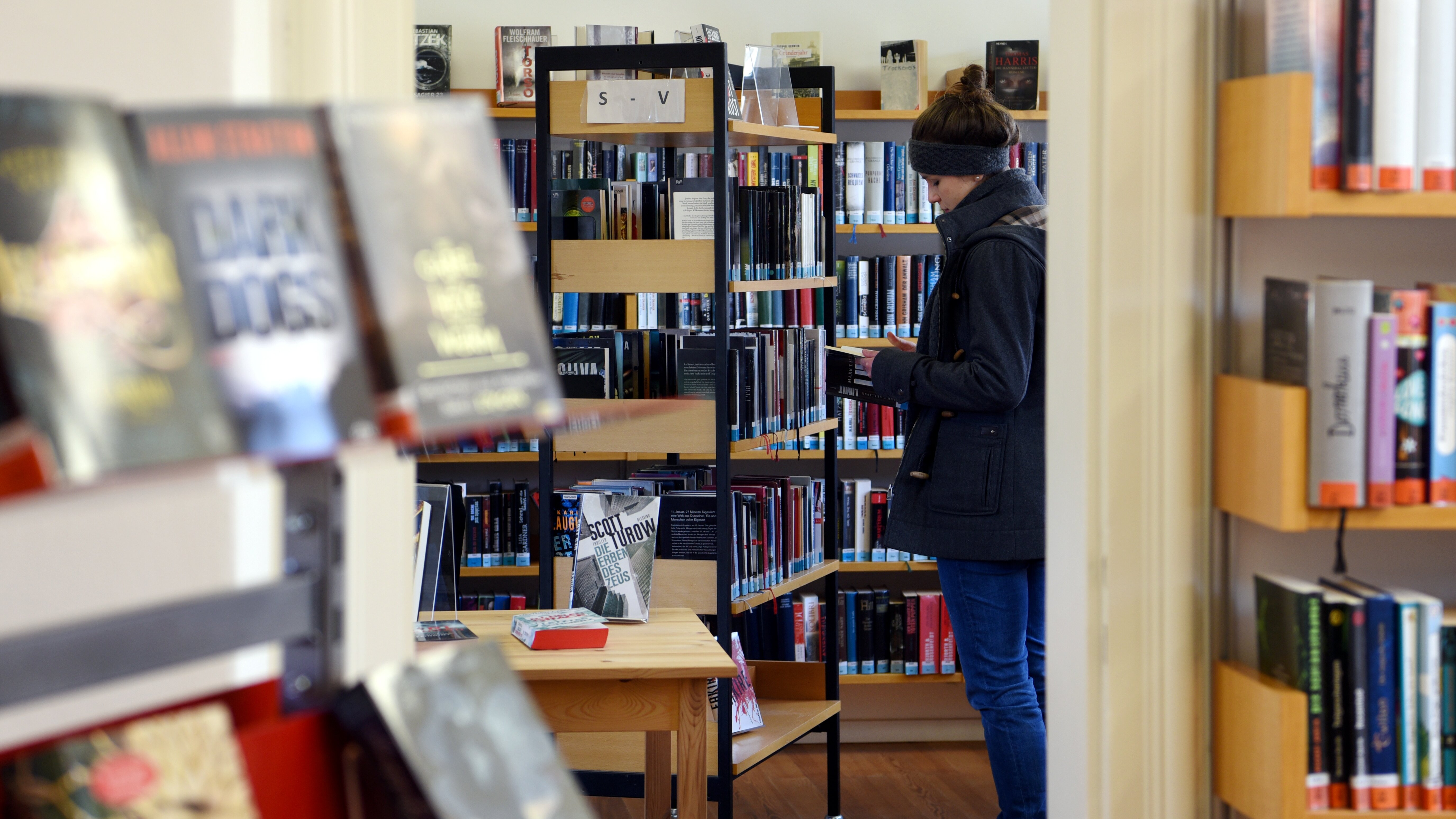 Innenansicht der Stadtteilbücherei Göggingen. Eine Frau schmökert zwischen den Regalen.