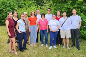 Gruppenfoto vor Bäumen auf einer Wiese mit 12 Personen die versetzt nebeneinander stehen