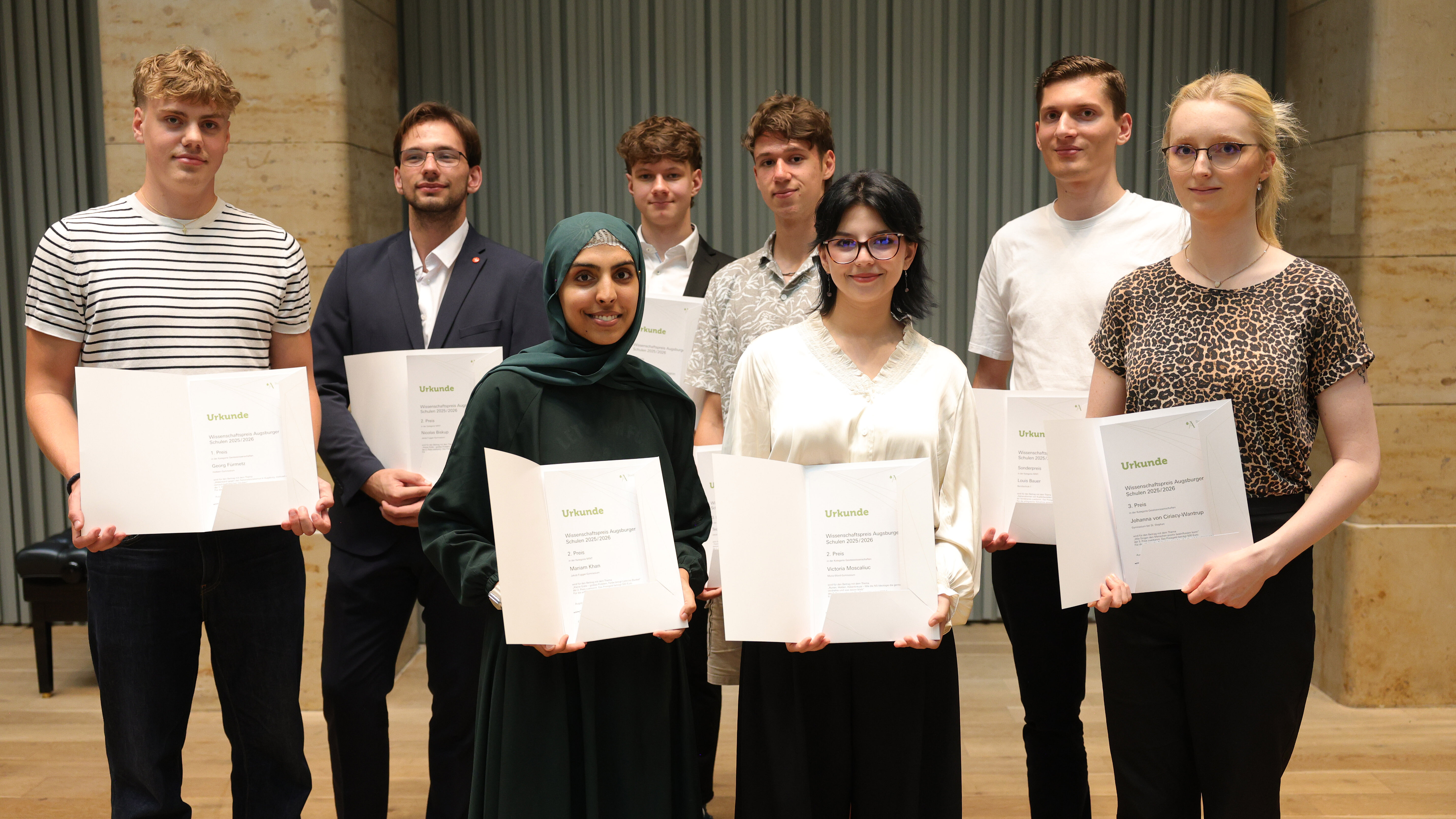 Das Bild zeigt 7 Schülerinnen und Schüler. In der hinteren Reihe stehen vier junge Männer, in der vorderen Reihe drei junge Frauen. Alle halten eine Urkunde in die Kamera und lächeln 