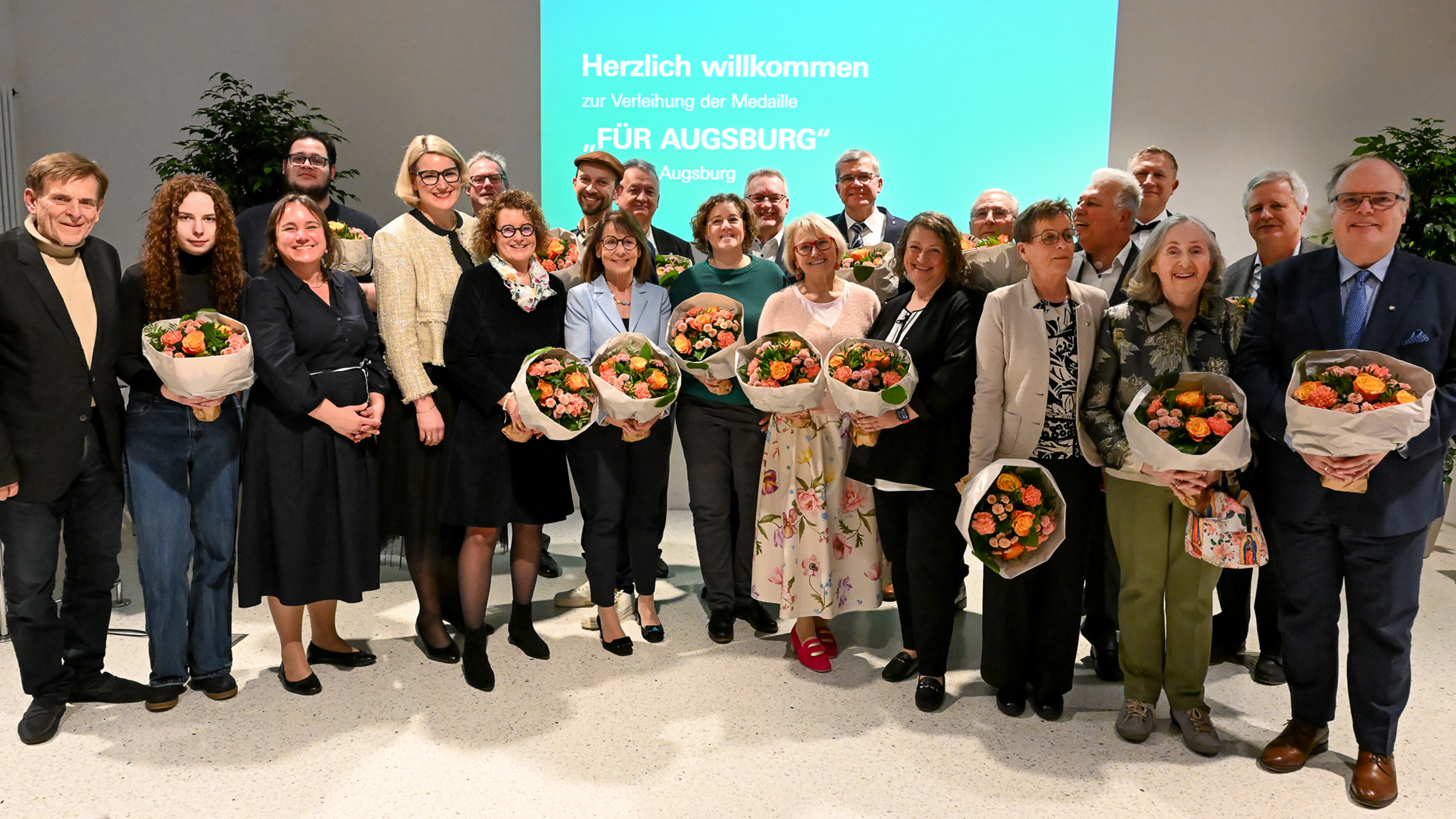 Etwa 20 Menschen in festlicher Kleidung, viele haben einen Blumenstrauß in der Hand