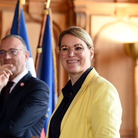 Ein Mann und eine Frau vor der deutschen und der französischen Flagge im Rathaus