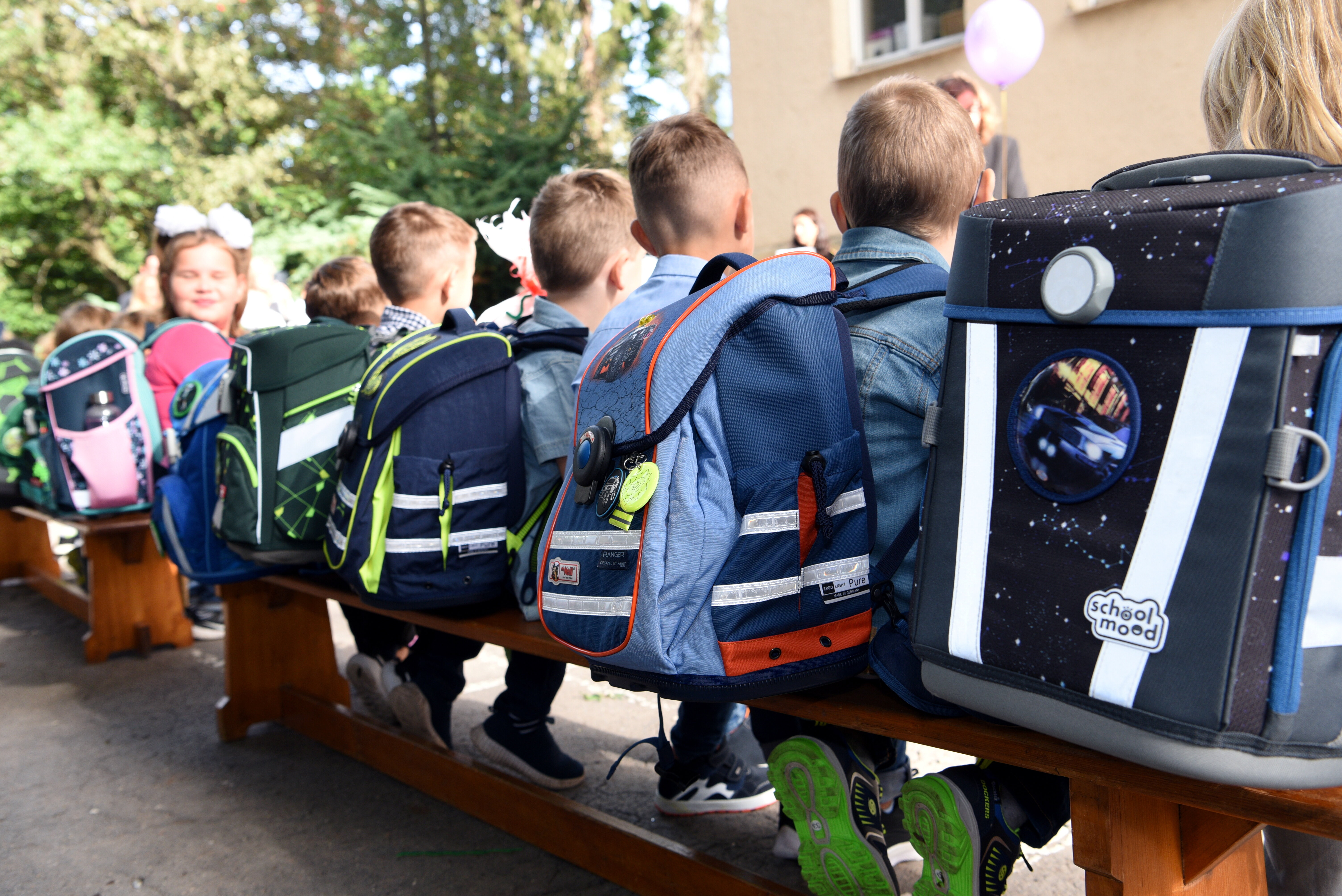 Schüler sitzen auf einer Bank, sie sind von hinten zu sehen. Vor allem die Schulränzen sind im Vordergrund.