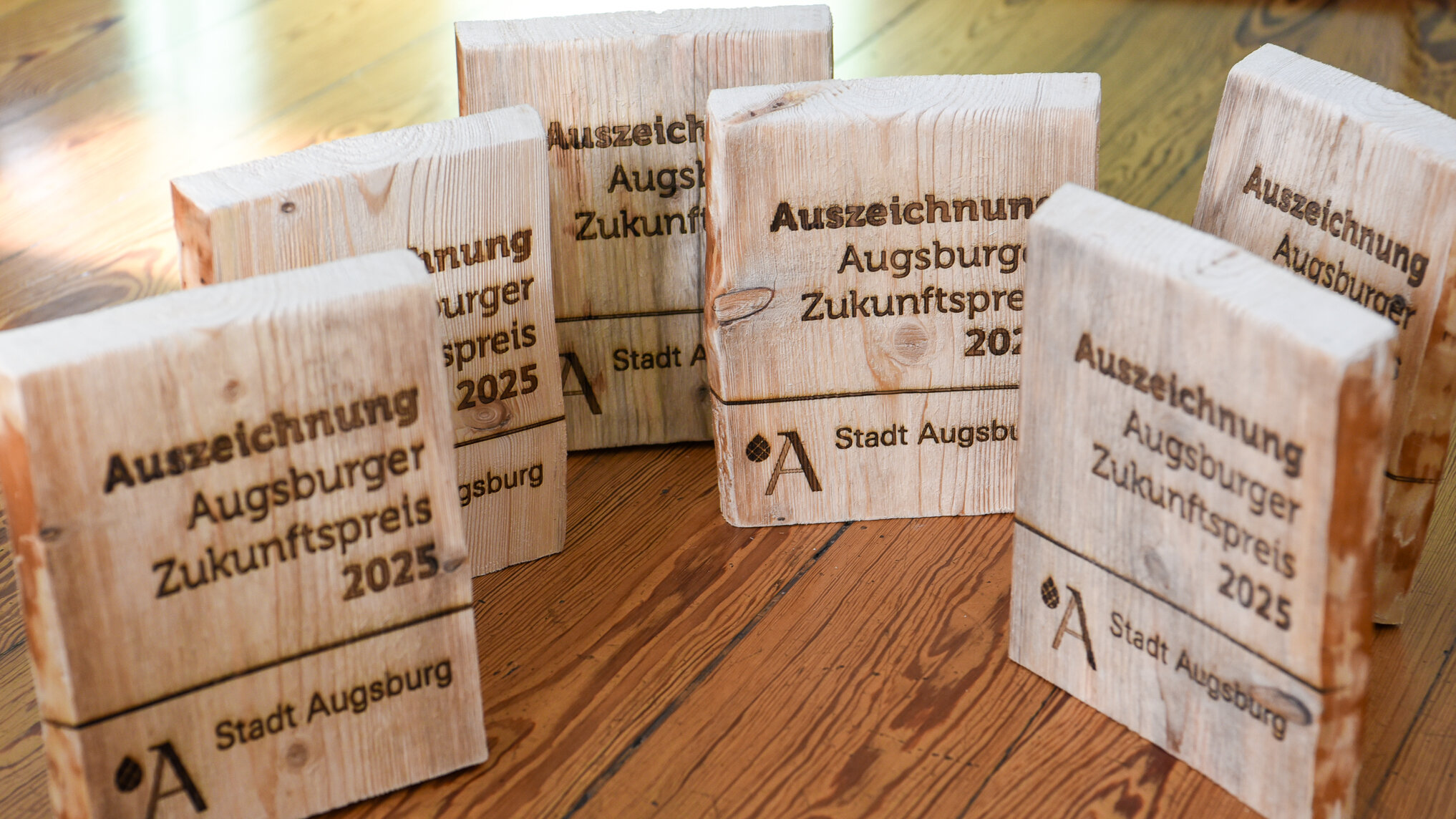 Holzelemente mit eingebrannter Schrift: Auszeichnung Augsburger Zukunftspreis 2025 Unterstrich darunter Stadt-Augsburg-Logo