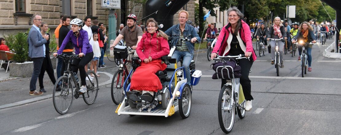 Das Bild zeigt die lange Radlnacht in Augsburg in der viele Fahrradfahrerinnen und Fahrradfahrer zu sehen sind, darunter eine Person im Rollstuhltransportfahrrad.