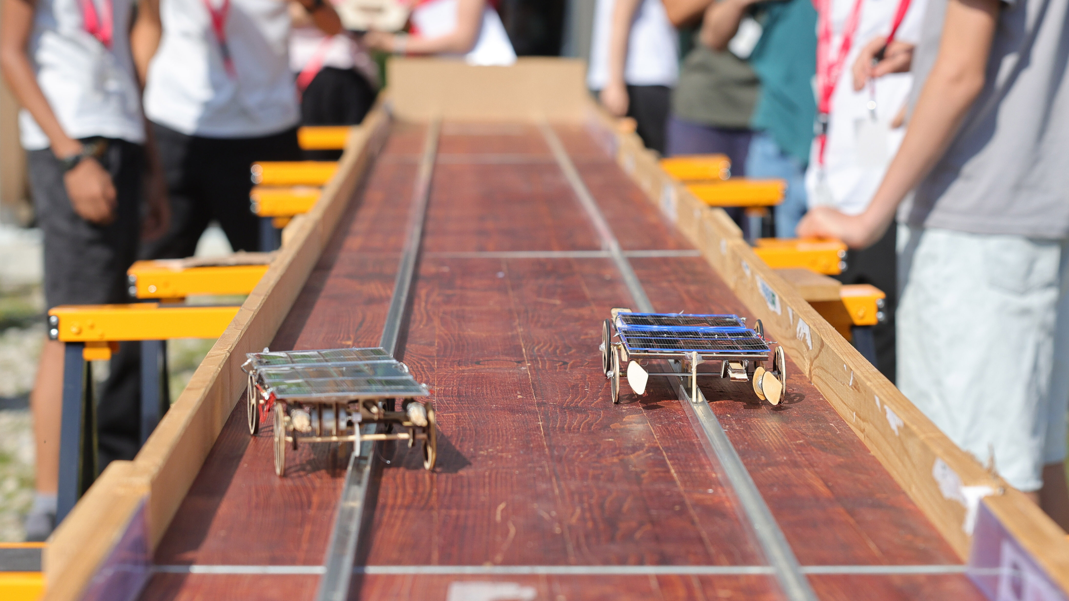 Zwei einfache Solarautomodelle auf einer hölzernen Rennbahn.