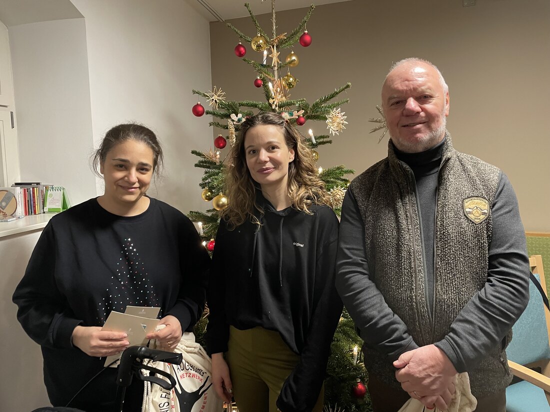 Zwei Frauen und ein Herr stehen vor einem Weihanchtsbaum.