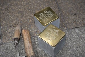 Blick von oben auf zwei Stolpersteine aus Messing; daneben ein Hammer