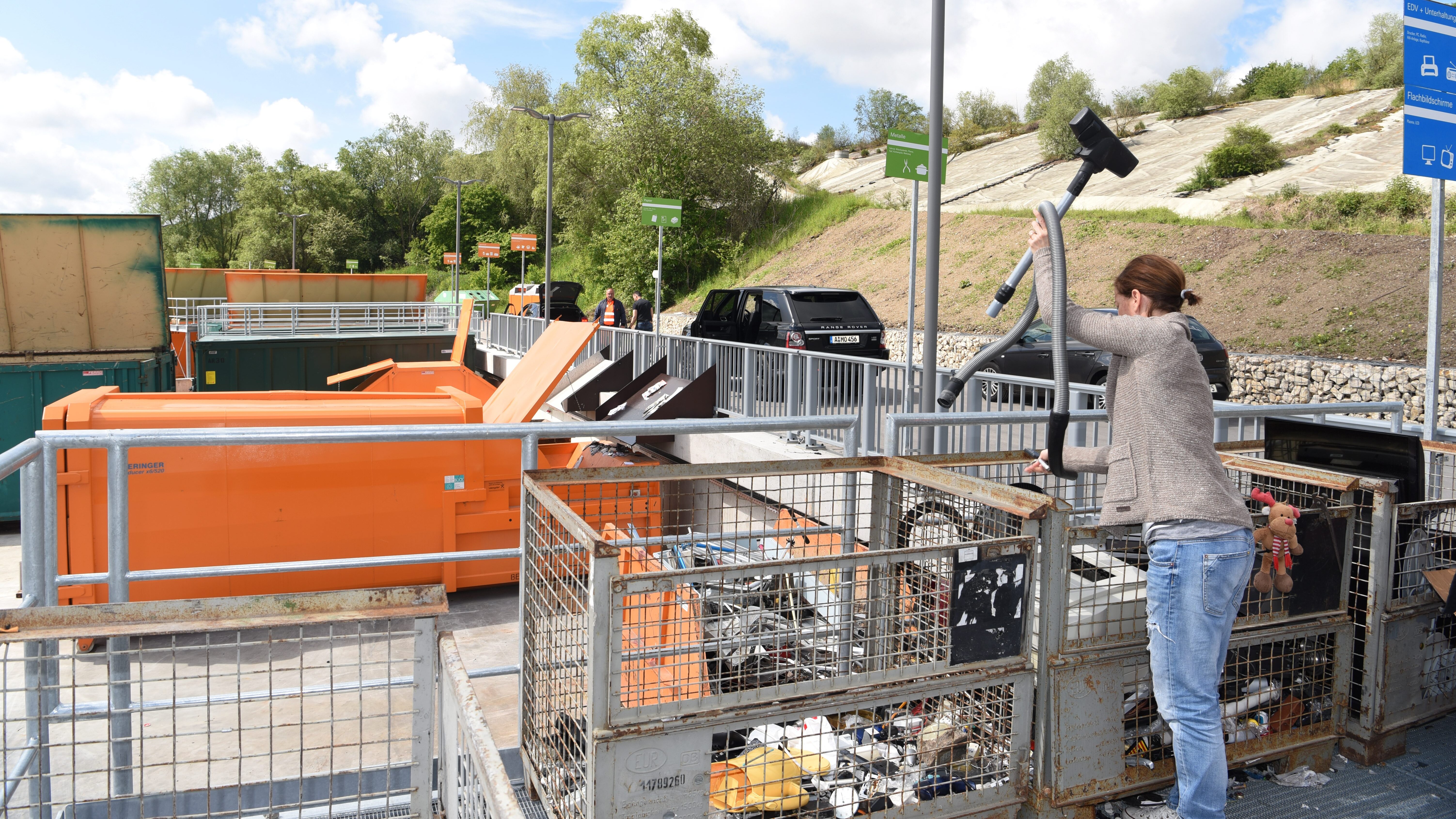 Eine Frau wirft einen Staubsauger in einen Müllcontainer