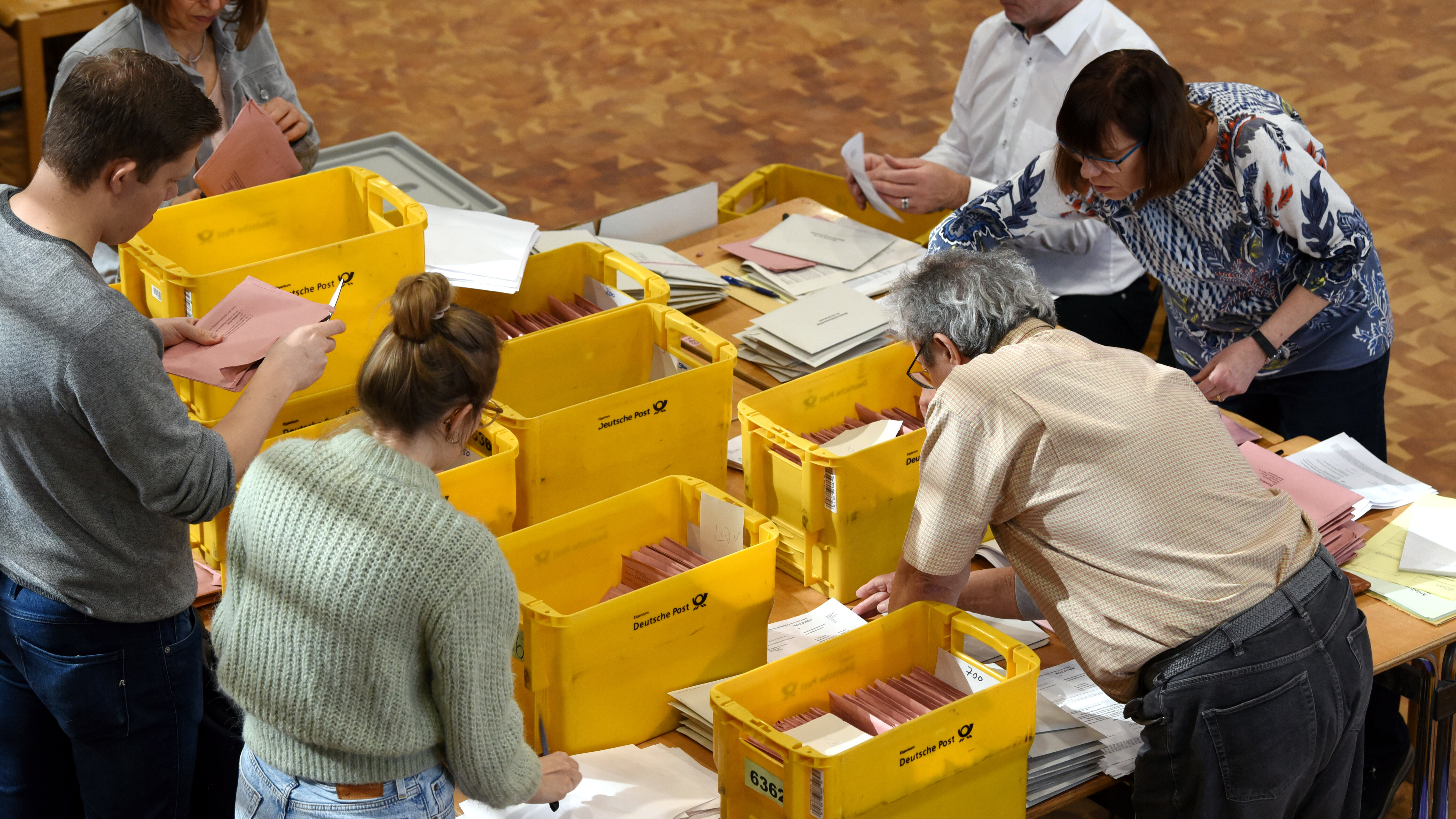 Einige Menschen stehen um einen Tisch mit vielen Postkisten. Sie sortieren Papiere