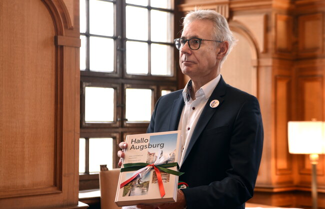 Ein Mann hält ein Buch mit der Aufschrift "Hallo Augsburg"