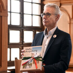 Ein Mann hält ein Buch mit der Aufschrift "Hallo Augsburg"